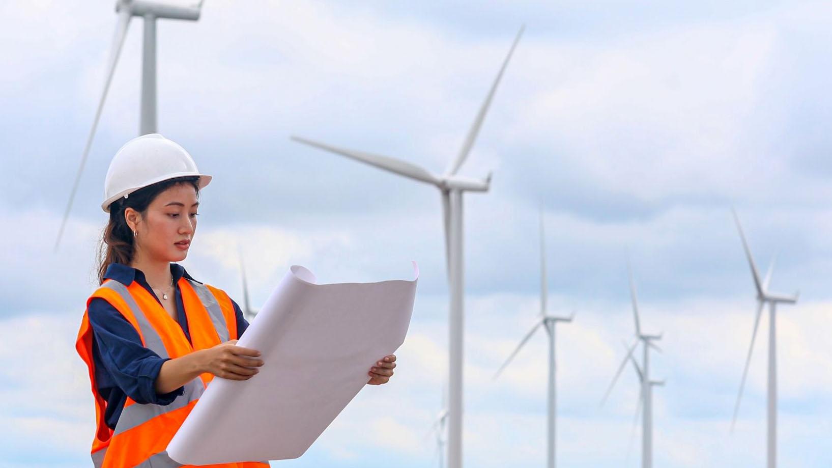 Image of woman looking at plans in front of wind turbines